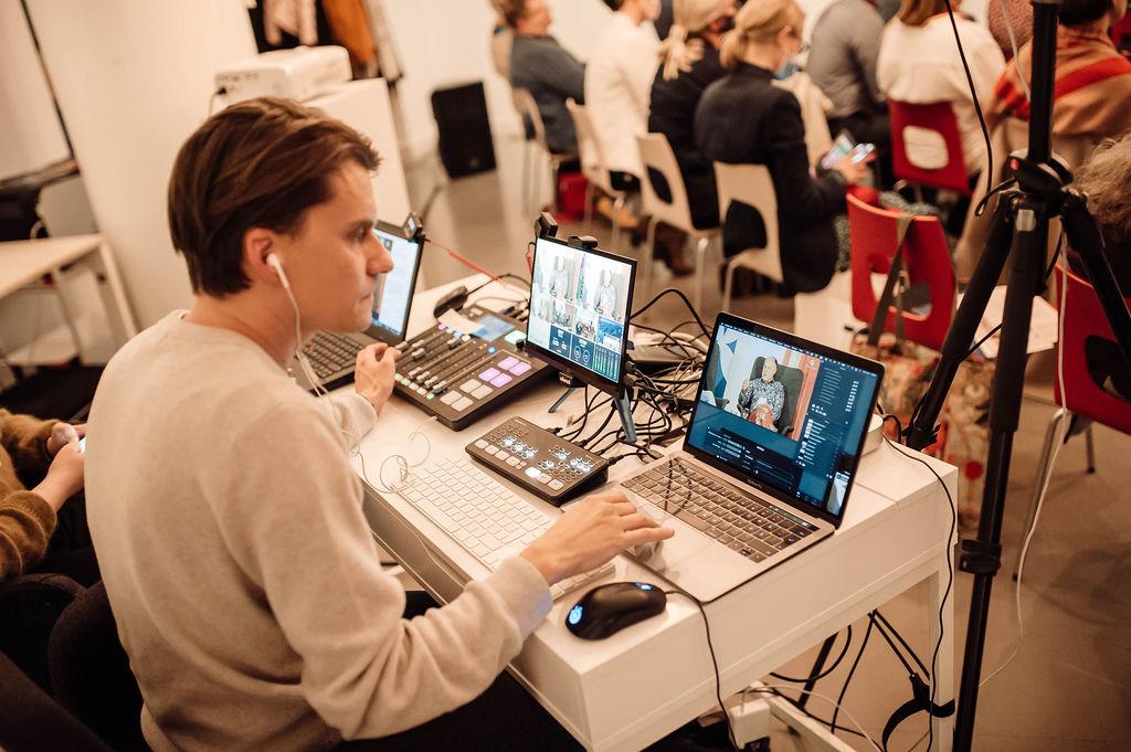 En man som sänder live ett evenemang. Han sitter vid ett bord med datorer och annan teknik framför sig.